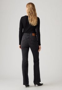 Jean flare noir à taille haute, avec un patch en cuir à l'arrière et un détail discret de couture sur la poche arrière. Texture denim lisse.