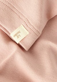 Miękka różowa bawełniana tkanina o prążkowanej fakturze; posiada wszywkę przyszytą w rogu. Widoczne szwy dodają szczegółów projektowi.