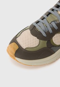Sportlicher Sneaker mit einer Kombination aus olivgrünem und taupefarbenem Mesh und Leder, grauen Schnürsenkeln und einer strukturierten Gummisohle.
