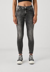 Grå skinny jeans med et falmet design, høj talje og frynset kant. Sammen med sorte og hvide low-top sneakers.