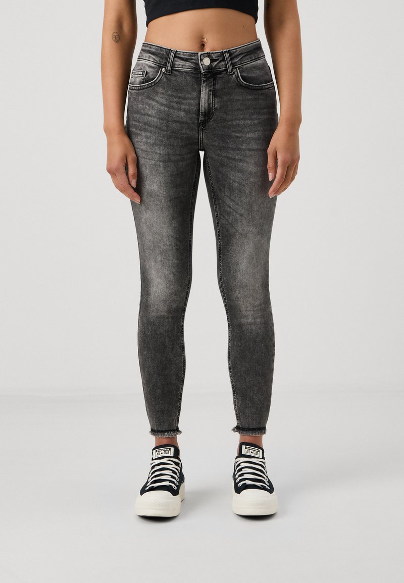 Grå skinny jeans med et falmet design, høj talje og frynset kant. Sammen med sorte og hvide low-top sneakers.