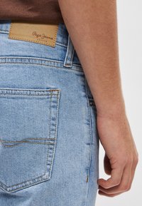 Ανοιχτό μπλε τζιν με ορατή ραφή, πίσω τσέπη και ταμπέλα από ταμπά δέρμα με το λογότυπο στη μέση. Κανονική εφαρμογή.