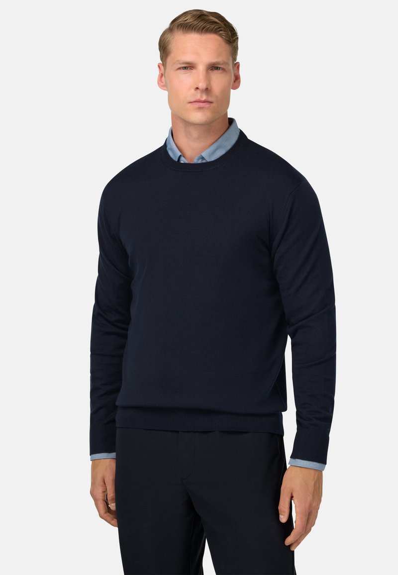 Suéter azul marino con cuello redondo y mangas largas, hecho de un material suave, superpuesto a una camisa de color azul claro con cuello.