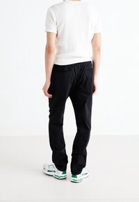 Svarta byxor med elastisk midja och två bakfickor, tillsammans med en krämfärgad ribbad kortärmad tröja och färgglada sneakers.