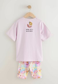 Gaiši violets kokvilnas T-krekls ar ziedu grafiku un tekstu, kopā ar pasteļtoņu ziedu raksta šortiem rozā, dzeltenā un zilā krāsā.