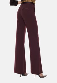 Pantaloni a gamba larga in tessuto bordeaux scuro, caratterizzati da una superficie liscia, tasca posteriore e abbinati a scarpe con tacco alto.