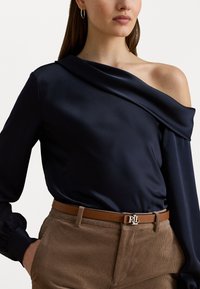 Marine satijnen blouse met een asymmetrisch, off-the-shoulder ontwerp, gecombineerd met tan corduroy broek en een lichtbruine riem met een zilveren RL-logo.