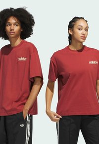 Červené bavlněné trička s logem "adidas basketball". Volný střih, krátké rukávy, v kombinaci s černými kalhotami a bílými pruhy.