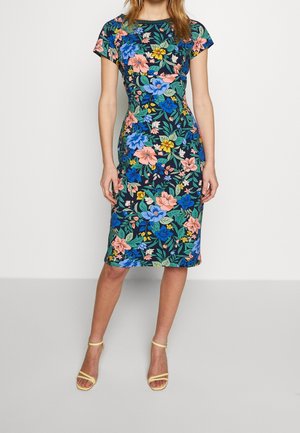 Vrouw draagt een nauwsluitende knie-lange jurk met bloemenprint, korte mouwen en multikleurige bloemen in blauw, roze, geel en groen op een donkere achtergrond.