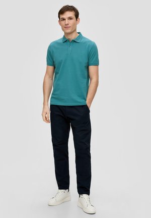 Teal polo shirt met een kraag, korte mouwen en een gestructureerde stof, gecombineerd met donkere marineblauwe broek en witte sneakers. Eenvoudig, modern ontwerp.
