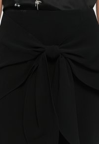 Black skirt featuring a prominent bow detail at the waist, made of smooth fabric with a structured design and layered folds.