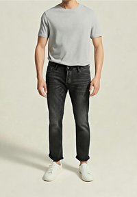 Maglietta grigia a maniche corte abbinata a jeans neri aderenti e sneakers bianche. Materiale in cotone, design casual, vestibilità standard e risvolti sulle maniche.