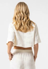 Top bianco corto con maniche corte, caratterizzato da un tessuto testurizzato. Abbinato a pantaloni chiari con vita elastica.