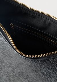 Μαύρη τσάντα από δέρμα με υφή, με ανοιχτό χρυσό φερμουάρ που αποκαλύπτει το εσωτερικό με μαύρο ύφασμα και εσωτερική τσέπη με φερμουάρ.