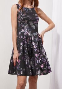Czarna sukienka w kwiatowy wzór w odcieniach fioletu i srebra. Bez rękawów, dopasowana góra, plisowana spódnica i fakturowany materiał.