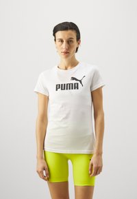 Hvid kortærmet t-shirt med et sort PUMA-logo, parret med lyse neongule tætsiddende shorts med strukturerede detaljer.