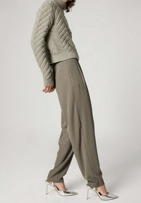 Hellgrauer, gestrickter Pullover mit hohem Kragen und strukturiertem Muster, kombiniert mit lockeren olivgrünen Hosen und silbernen Schuhen mit Absatz.