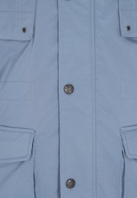 Jasnoniebieska kurtka o gładkiej teksturze, z podwójnymi kieszeniami klapowymi i metalowymi zatrzaskami. Szwy są widoczne wzdłuż krawędzi.