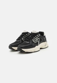 Baskets noires avec des tiges en mesh et en cuir, design irrégulier, accents crème et semelles en caoutchouc épaisses. Comprend des lacets blancs et un logo sur la languette.