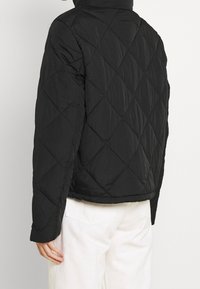 Sort quiltet jakke med høj krave, puffet tekstur og diamantmønster. Designet med en cropped længde og lange ærmer.
