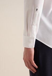 Camicia bianca con texture e polsini abbottonati, caratterizzata da una rosa nera ricamata sulla manica. Presenta una finitura liscia e un design aderente.