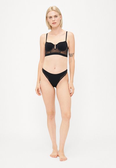 Zwarte bralette met transparante details en verstelbare bandjes, gecombineerd met bijpassende hoogsluitende bikini broekjes, beide met verfijnde stiksels.