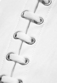 Gros plan d’un tissu blanc avec des lacets blancs enfilés dans des œillets métalliques en motif zigzag.
