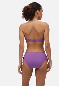 Top de bikini morado con diseño sin tirantes y parte inferior ajustable con lazo. Textura suave, color vibrante, hardware mínimo.