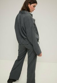 Szara bawełniana koszula w oversize'owym stylu i dopasowane spodnie, charakteryzujące się luźnym krojem, długimi rękawami oraz minimalistycznym wzornictwem z fakturami.