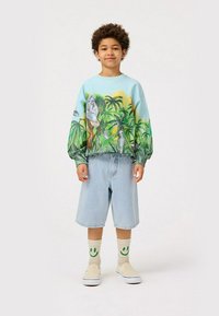 Felpa celeste con stampa tropicale, polsini elasticizzati, pantaloncini in denim, scarpe slip-on beige e calze con faccina sorridente. Outfit casual per un bambino.