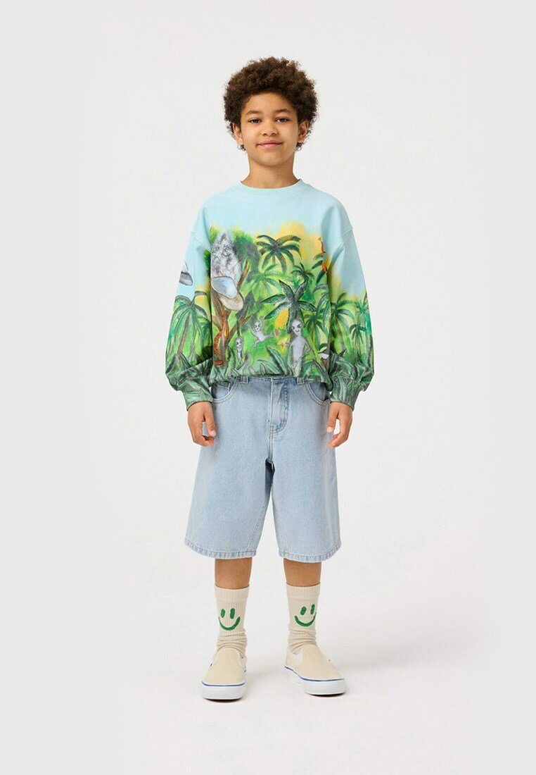 Felpa celeste con stampa tropicale, polsini elasticizzati, pantaloncini in denim, scarpe slip-on beige e calze con faccina sorridente. Outfit casual per un bambino.