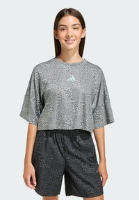 Krátky sivý top s krátkym rukávom, leopardím vzorom a tyrkysovým logom, v kombinácii s čiernymi šortkami s podobným leopardím vzorom.