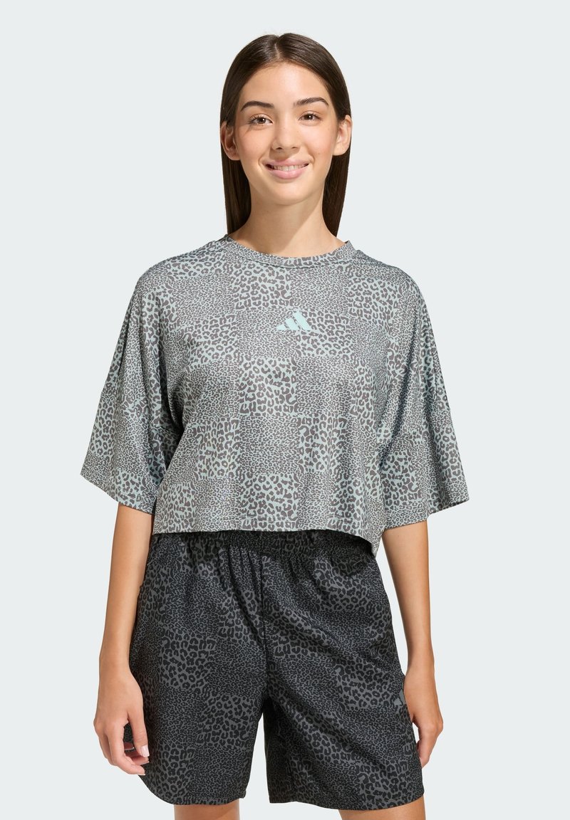 Krátky sivý top s krátkym rukávom, leopardím vzorom a tyrkysovým logom, v kombinácii s čiernymi šortkami s podobným leopardím vzorom.
