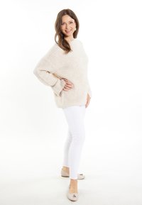 Ljusbeige stickad tröja med ribbad textur, ihop med vita slim fit-jeans och beige ballerina med dekorativ detalj.