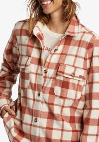 Red and cream plaid flannel shirt with a collar, button closure, two chest pockets, and a soft, textured finish.
