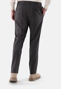 Graue Wollhosen mit taillierter Passform, ausgestattet mit zwei Gesäßtaschen und einem gefalteten Vorderteil, kombiniert mit hellen Schuhen.