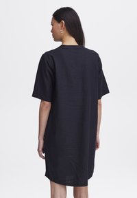 Tmavomodré oversized tričko šaty vyrobené z jemnej látky, s okrúhlym výstrihom, krátkymi rukávmi a zaobleným lemom.