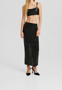 Svart crop-top i glansigt material, kombinerad med en lång, smal svart kjol prydd med vita prickar. Utrustad med svarta spetsiga klackar.