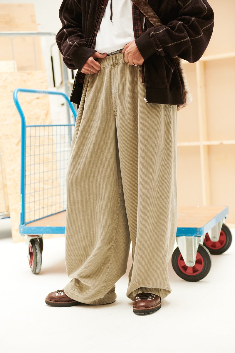 Bézs kordbársony széles szárú nadrág elasztikus derékpánttal, sötétbarna cipőkkel, amelyek fémes díszítésekkel rendelkeznek.