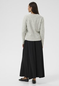 Lichtgrijze gebreide sweater met een ronde hals, gecombineerd met een lange zwarte rok. De outfit heeft een zachte textuur en een casual silhouet.