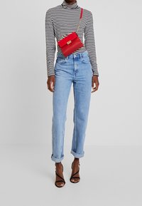 Röd läder crossbody-väska med kedjerygg, rektangulär form, med guldfärgad hårdvara och nitar. Buren med randig polotröja och jeans.