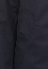 Mørkeblå stof med en tekstureret finish, der har en sidelomme med en smal åbning, designet til praktisk brug.