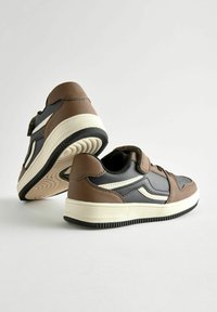 Ruskeat ja mustat lenkkarit, joissa on sileä nahka ja tekstiilimateriaalit. Varustettu valkoisella sivuviivalla, velcro-kiinnityksellä ja kuvioidulla kumipohjalla.
