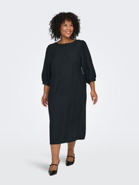 Musta midi-mekko, jossa on pehmeää, laskeutuvaa kangasta. Pyöreä kaula-aukko ja pullistetut ¾-hihat. Yhdistetty mustien, teräväkärkisten balleriinojen kanssa.