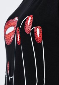 Černé tričko s grafickým motivem červených rtů a prodloužených prstů, zdobené červenými rhinestones a obrysem v bílé barvě. Měkká, elastická tkanina.