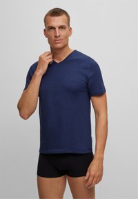 Navy blue cotton v-neck t-shirt with short sleeves, featuring a subtle logo on the chest and a relaxed fit. Worn with black shorts.