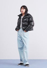 Sort pufferjakke med en blank finish, lagdelt over en grå top. Lys blå højtaljede jeans og sorte sneakers fuldender outfittet.