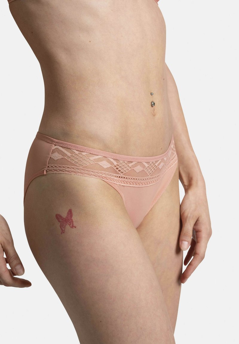 Culottes de bikini en couleur pêche avec des accents en dentelle à la taille, présentant une texture lisse et un motif décoratif en diamants.