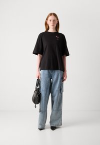 Black cotton t-shirt with a pink cocktail graphic, paired with light blue wide-leg jeans and a small black handbag.