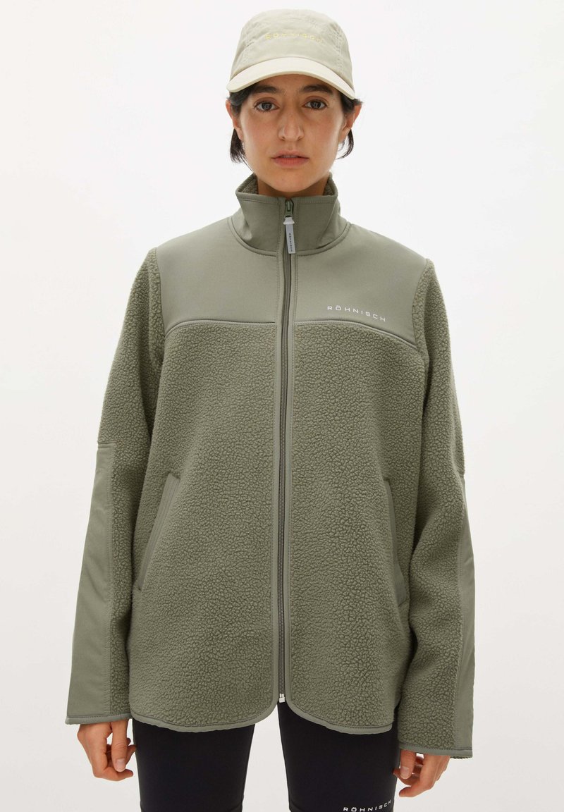 Giacca in fleece di colore verde oliva chiaro, con colletto alto, chiusura con zip e due tasche laterali. Tessuto morbido con pannelli lisci in contrasto.